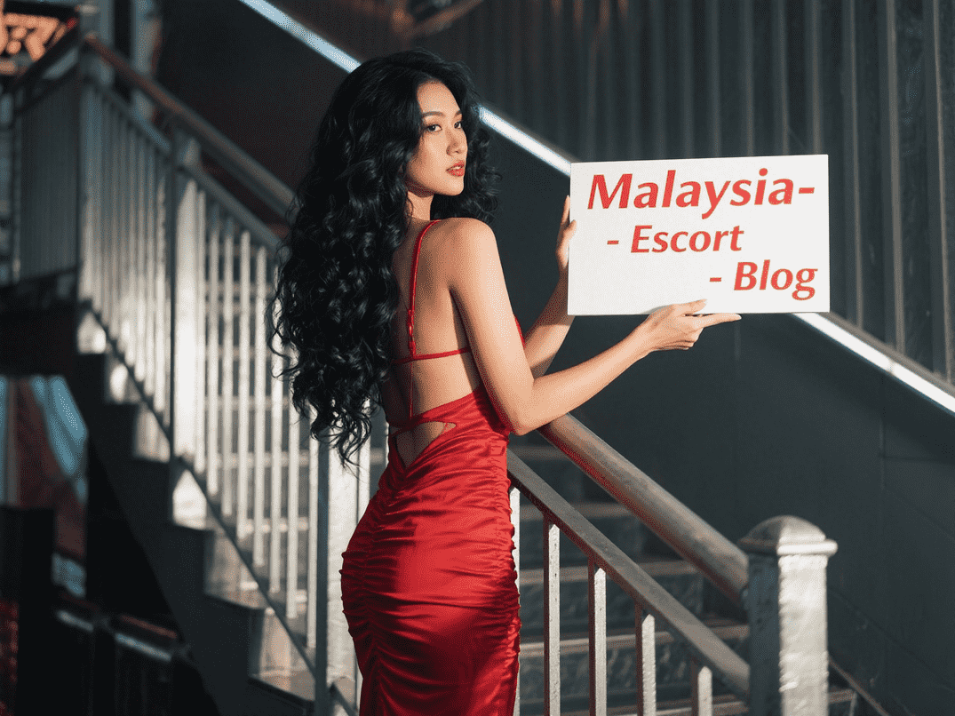 Woman in red dress holding "Malaysia-Escort-Blog" sign near stairs. KL Escort Outcall info.